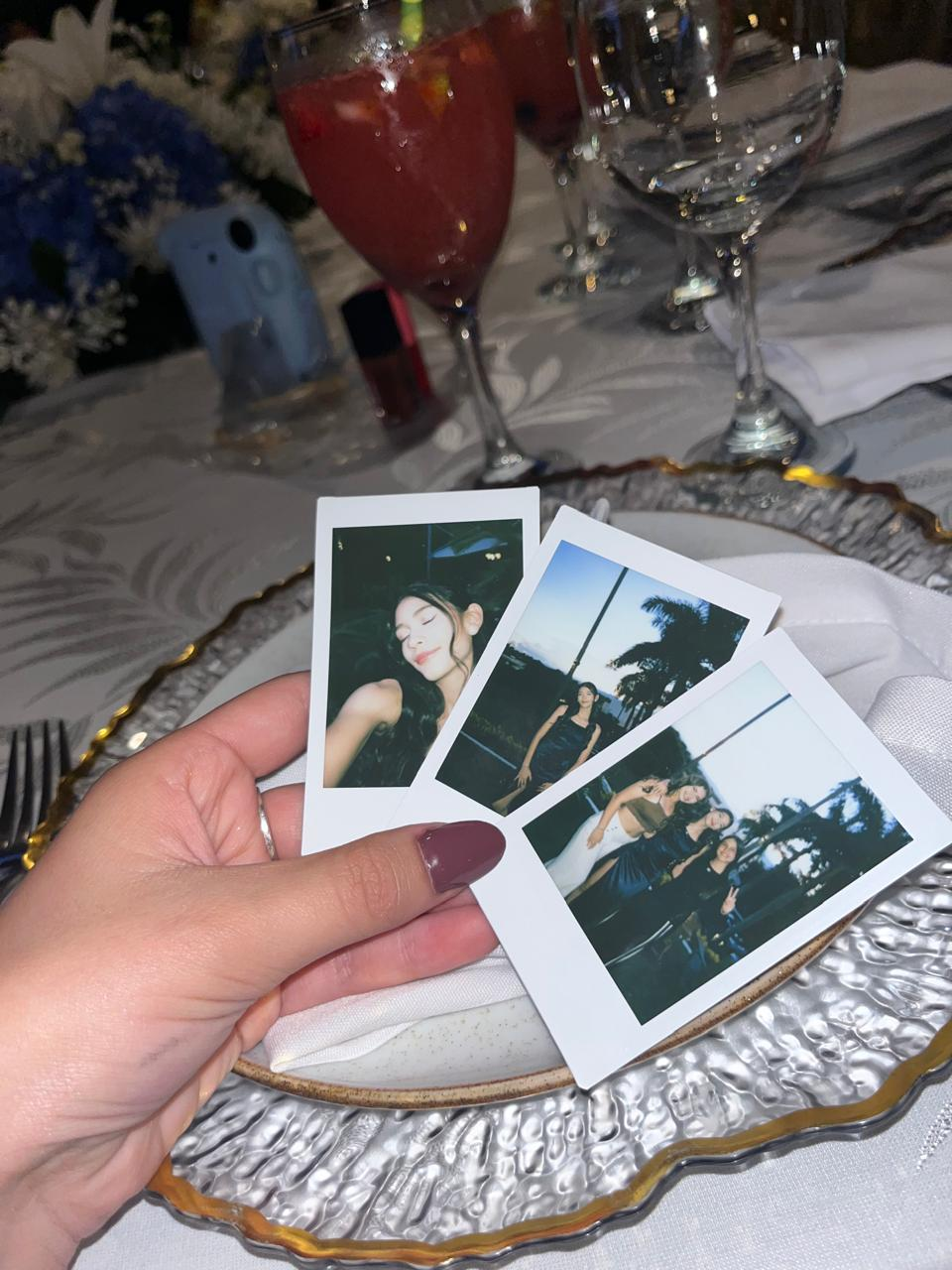 Mano sosteniendo tres fotografías tipo Polaroid sobre una mesa de celebración