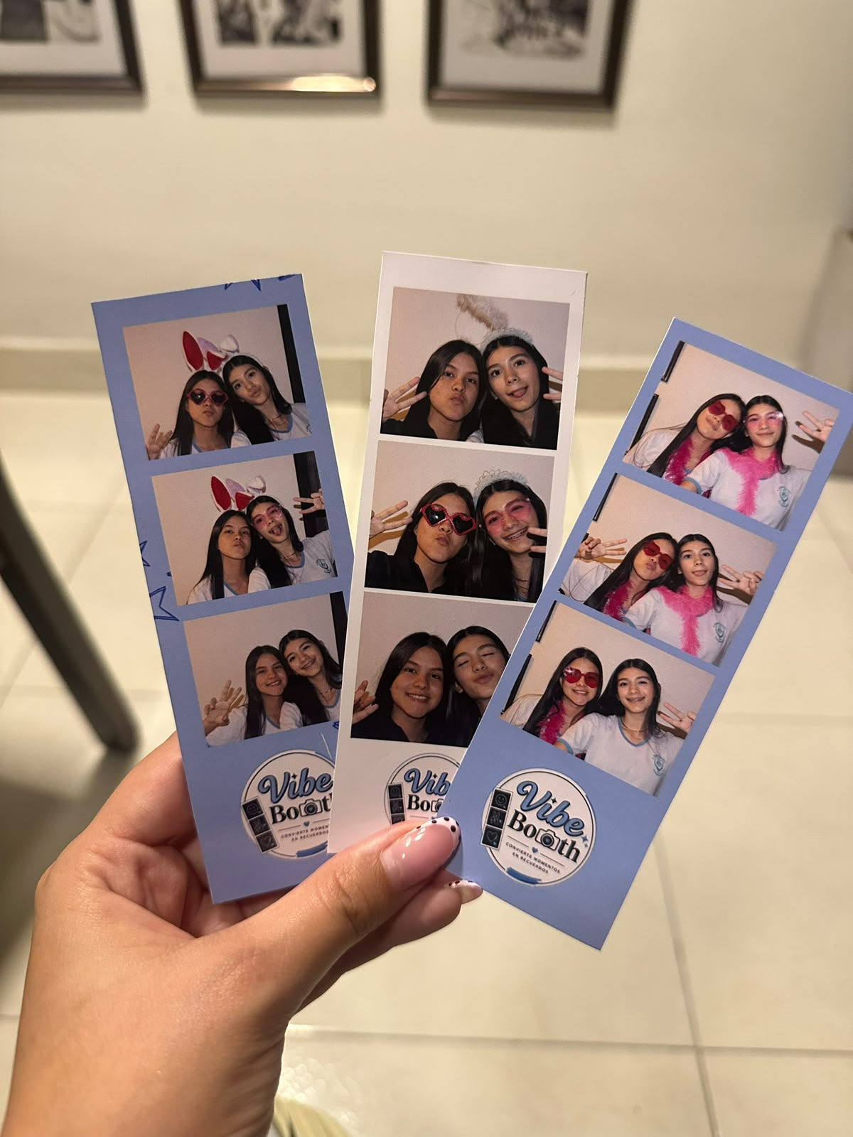 Mano sosteniendo tres tiras de fotos del photo booth con el logo de Vibe Booth